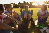 Вид спереду виснажених різноманітних футболісток, які сидять на полі і розмовляють один з одним на спортивному полі . — стокове фото