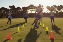 Vista frontal de diversas jugadoras de fútbol que pasan la pelota entre los conos durante el entrenamiento en el campo - foto de stock