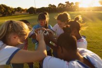 Vista de ángulo alto del diverso equipo femenino de fútbol animando en círculo con pelota en el campo de deportes - foto de stock