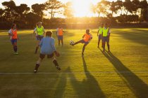 Vue de face de diverses joueuses de soccer jouant sur un terrain de sport au crépuscule — Photo de stock
