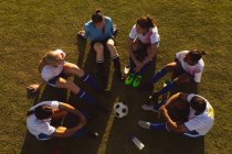 High angle view of exhausted diverse female soccer players sitting in a circle and talking to each other on the field — Stock Photo