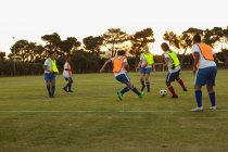 Vista posteriore di diverse giocatrici di calcio che giocano a calcio al campo sportivo al tramonto
. — Foto stock