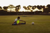 Vista lateral de una futbolista afroamericana haciendo ejercicios de calentamiento en el campo de deportes durante el torneo - foto de stock