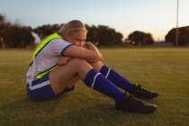 Vista lateral do jogador de futebol feminino caucasiano relaxando na grama no campo de esportes — Fotografia de Stock