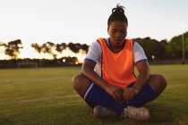 Front view of African-american female soccer player relaxing on grass at sports field — Stock Photo