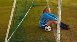 Vista lateral del reflexivo jugador de fútbol femenino caucásico relajándose en el campo de deportes - foto de stock