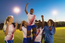 Vista frontal da equipe de futebol feminino diversificada torcendo por sua vitória no campo esportivo — Fotografia de Stock
