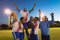 Вид спереду на різноманітну жіночу футбольну команду, яка вітає перемогу на спортивному полі — стокове фото