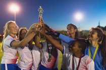 Vista frontal del diverso equipo femenino de fútbol que sostiene el trofeo después de ganar el juego en el campo de deportes - foto de stock