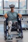 Вид спереди кавказской пациентки-инвалида с помощью гарнитуры виртуальной реальности в инвалидной коляске в больнице — стоковое фото