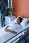 Hochwinkelaufnahme einer Patientin mittleren Alters mit gemischter Rasse, die mit den Händen auf dem Bauch im Bett auf der Station des Krankenhauses schläft — Stockfoto