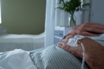 Mid section of male patient lying in bed with hands on his chest in the ward in hospital. He is getting intravenous therapy. — Stock Photo