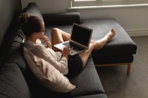 Vista alta da mulher caucasiana usando laptop em um sofá na sala de estar em casa — Fotografia de Stock
