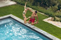 Vista alta de pareja caucásica saltando juntos en la piscina en el patio trasero - foto de stock