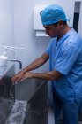 Vista lateral del guapo cirujano caucásico lavándose las manos con jabón en el lavabo en el hospital - foto de stock