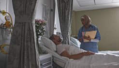 Visão frontal de uma médica mista interagindo com um paciente caucasiano do sexo masculino na enfermaria do hospital . — Fotografia de Stock