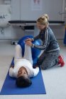 Visão lateral de fisioterapeuta feminina branca dando fisioterapia a paciente mestiça em exercício no hospital — Fotografia de Stock
