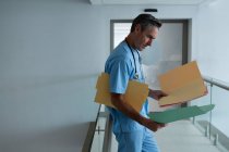 Вид на симпатичного взрослого врача-белого мужчину со стетоскопом вокруг шеи, смотрящего на отчет в коридоре больницы — стоковое фото