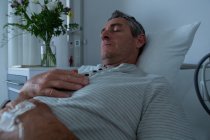 Vorderseite des friedlichen reifen kaukasischen männlichen Patienten, der im Bett schläft, mit der Hand auf der Brust auf der Station im Krankenhaus — Stockfoto
