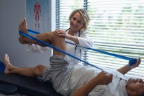 Vorderansicht einer kaukasischen Ärztin, die im Krankenhaus das Bein eines älteren Mischlingspatienten mit Widerstandsband untersucht — Stockfoto
