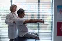 Побочный обзор взрослой белой женщины-врача, осматривающей пожилого пациента смешанной расы в больнице — стоковое фото