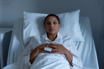 Retrato de bela jovem mestiça paciente do sexo feminino deitado na cama com as mãos no estômago na enfermaria no hospital. A oximetria de pulso está a medir o nível de oxigénio no sangue. . — Fotografia de Stock