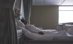 Vue latérale d'une patiente mature de race mixte dormant au lit dans la salle d'hôpital — Photo de stock