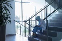 Боковой вид женщины-врача смешанной расы в хиджабе, пишущей на планшете на лестнице в больнице — стоковое фото