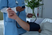 Sección media del médico femenino que revisa la presión arterial del paciente masculino en la sala del hospital - foto de stock