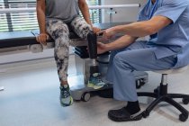 Sección baja del fisioterapeuta masculino ajustando la pierna protésica de la paciente femenina en el hospital - foto de stock