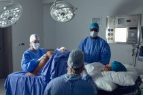 Visão lateral de diversos cirurgiões examinando a mulher grávida durante o parto, enquanto o homem caucasiano segurando a mão na sala de cirurgia no hospital — Fotografia de Stock