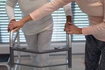 Низька секція жіночого фізіотерапевта, який допомагає пацієнтці змішаної раси ходити з ходунками в лікарні — стокове фото