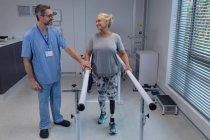 Vista frontale del fisioterapista maschile caucasico che aiuta il paziente a camminare con barre parallele in ospedale — Foto stock