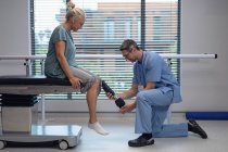 Visão lateral do fisioterapeuta masculino caucasiano ajustando a perna protética da paciente do sexo feminino no hospital — Fotografia de Stock