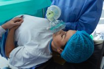 Vista lateral del cirujano que reconforta a la mujer embarazada durante el parto en quirófano en el hospital - foto de stock