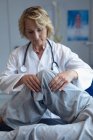 Vue de face du médecin féminin caucasien examinant les patients masculins genou à l'hôpital — Photo de stock