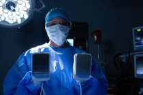 Portrait de jeune chirurgienne métisse tenant un défibrillateur en salle d'opération à l'hôpital . — Photo de stock