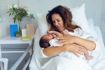 Visão frontal da bela mãe segurando seu filho recém-nascido após o parto na enfermaria do hospital — Fotografia de Stock