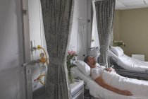 Vista laterale del paziente maschio caucasico che dorme con la mano sul petto nel letto nel reparto dell'ospedale — Foto stock