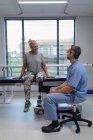 Vue latérale du kinésithérapeute masculin caucasien heureux parlant avec une patiente handicapée à l'hôpital — Photo de stock