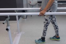 Baixa seção de paciente amputada do sexo feminino caminhando com barras paralelas no hospital — Fotografia de Stock