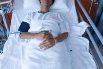Средняя часть пациентки смешанной расы лежит в постели, получая внутривенную терапию и пульсоксиметрию в палате больницы — стоковое фото