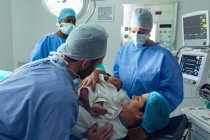 Вид збоку кавказької пари з хірургів проведення їх новонародженої дитини в театрі операцій в лікарні — стокове фото