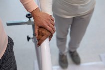 Закрытие женского физиотерапевта, помогающего пациентке смешанной расы ходить с параллельными решетками в больнице — стоковое фото