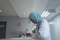 Vue latérale du médecin mixte féminin en hijab lisant les documents à la réception à l'hôpital — Photo de stock