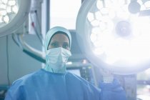 Портрет женщины-хирурга смешанной расы, держащей хирургический свет, стоя в операционной в больнице . — стоковое фото