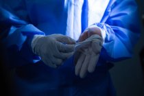 Средняя часть женского хирурга снимает хирургические перчатки в операционной — стоковое фото