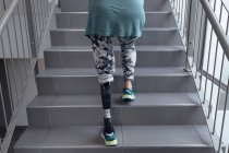 Sección baja de una paciente discapacitada con una pierna protésica que camina por las escaleras en el hospital - foto de stock