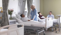 Frontansicht einer Krankenschwester mit gemischter Rasse, die mit einer Patientin interagiert, während verschiedene Paare neben ihnen auf der Station im Krankenhaus stehen. — Stockfoto