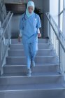 Вид спереду молодого лікаря змішаної раси в хіджабі, що йде вниз в лікарні — стокове фото